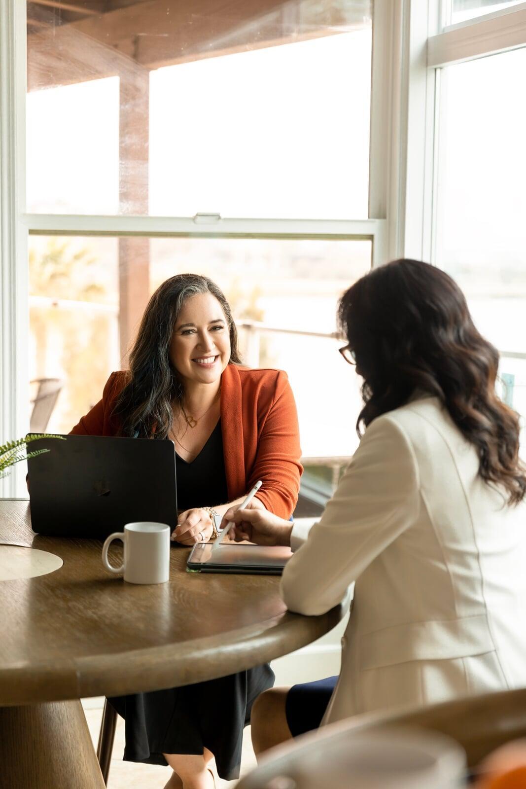 Benah Parker, Ph.D. in a deep orange blazer coaching a client in a bright, natural-lit office